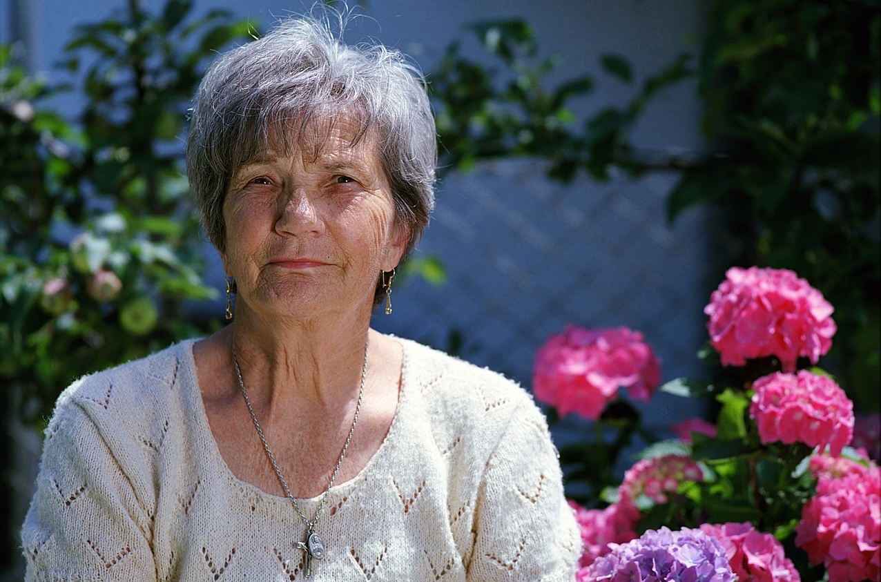 A lady smiling with flowers in the background.